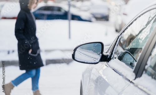 Car mirror in the snow with a pedestrian on the background. The concept of winter conditions on the road, ice and bad weather for driving vehicles.
