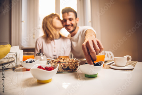 Young happy couple sitting by table having breakfast together at morning