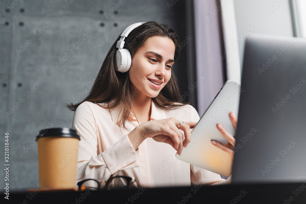 Millennial young woman enjoying great sound of music in wireless headphones. Great visual and audio content for channel subscribers. Girl typing on laptop and texting on smart tablet. Millennial young woman enjoying great sound of music in wireless headphones. Great visual and audio content for channel subscribers. Girl typing on laptop and texting on smart tablet.