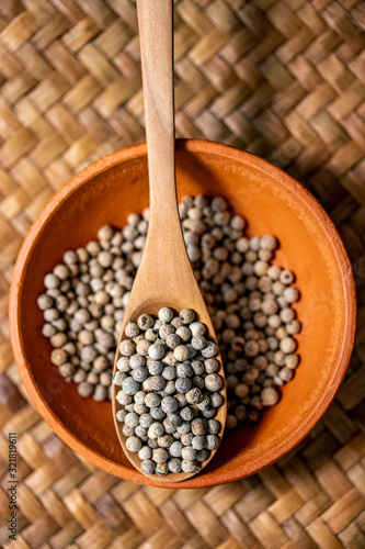 close-up of white pepper on wooden spoon in earthen bowl, most important flavorings in East Asia.