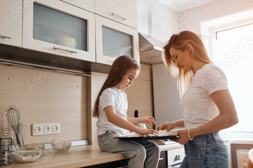 young mommy teaching her child to cook cookies in the kitchen with modern interior, close up side view photo, copy space. household chores, duties, traditions