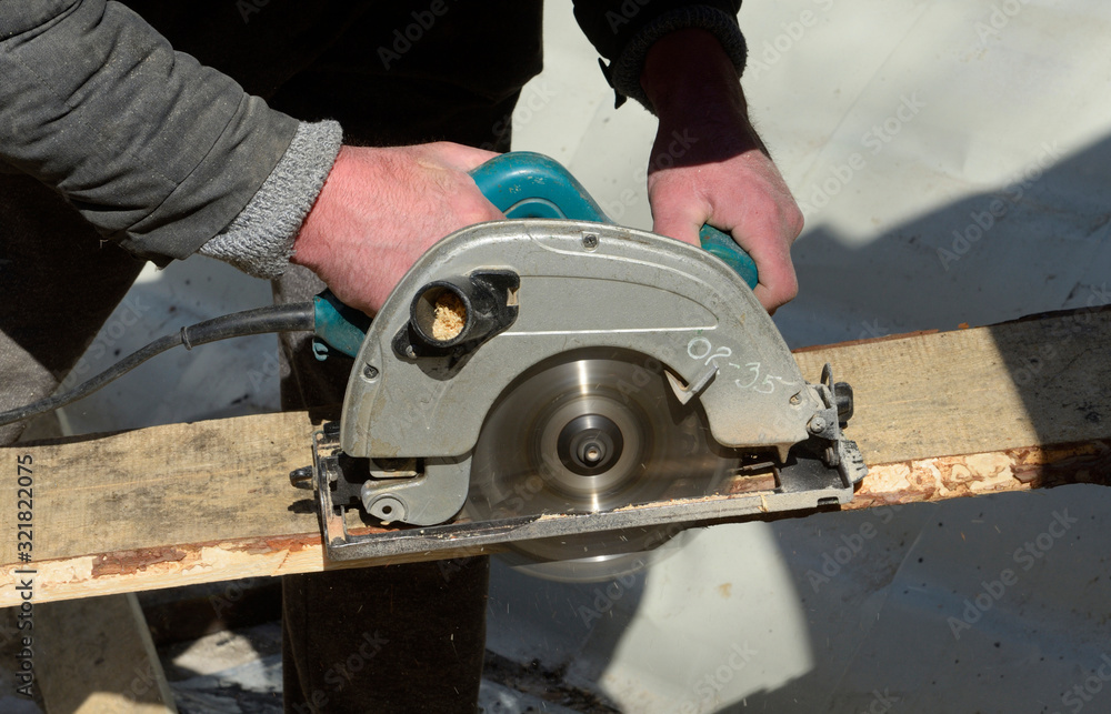 Joiner hands hold a circular saw cutting a board, close up Joiner hands hold a circular saw cutting a board, close up