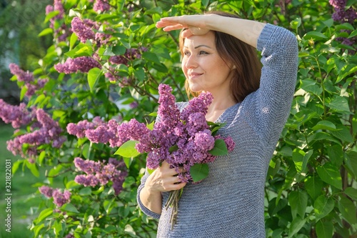 Portrait of mature smiling woman in garden with bouquet of lilacs © Valerii Honcharuk