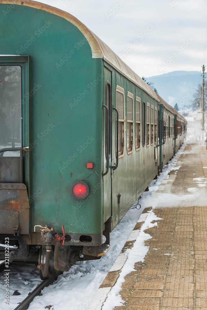 Obraz premium Velingrad railway station, Bulgaria - February 8, 2020: Train with red locomotive and green wagons departures at the train station.