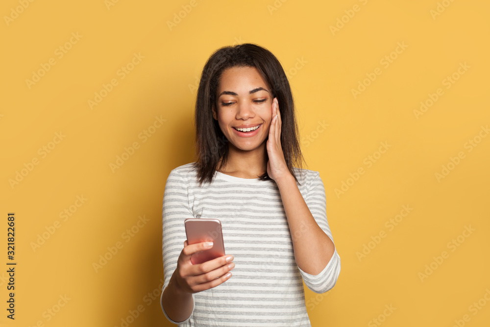 Cute black woman using cell phone and having fun on yellow Cute black woman using cell phone and having fun on yellow