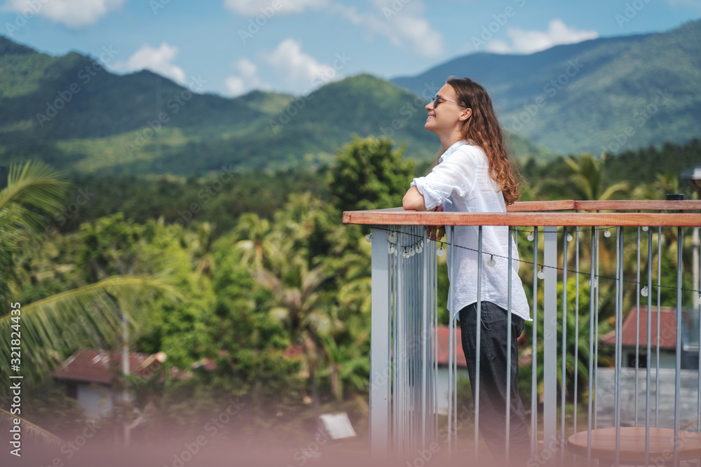 Happy young girl female traveler enjoying mountain and jungle view standing on terrace