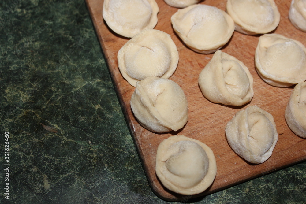 Dumplings on a wooden board on a green background. Top view on a green table with homemade food. Uncooked handmade dumplings on a wooden plate. Dumplings on a wooden board on a green background. Top view on a green table with homemade food. Uncooked handmade dumplings on a wooden plate.
