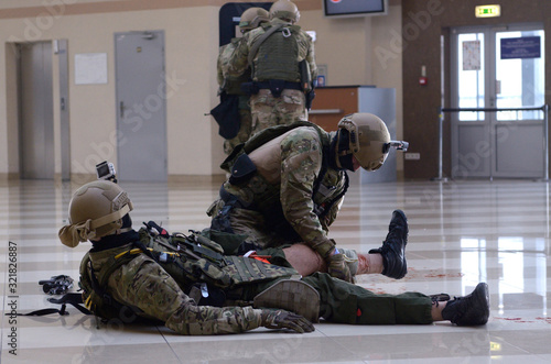 Fotografie Soldier of police strike force giving first aid to his wounded fellow, others to