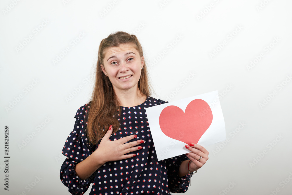 Fair-haired beautiful girl in a black dress with white circles holds piece of paper with heart shape Fair-haired beautiful girl in a black dress with white circles holds piece of paper with heart shape