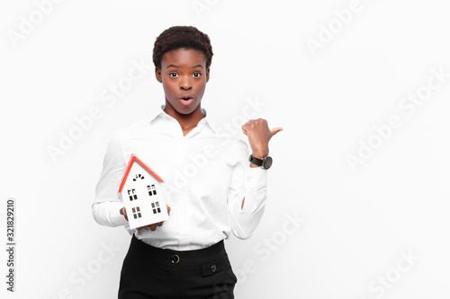 young pretty black womanlooking astonished in disbelief, pointing at object on the side and saying wow, unbelievable with a house model photo