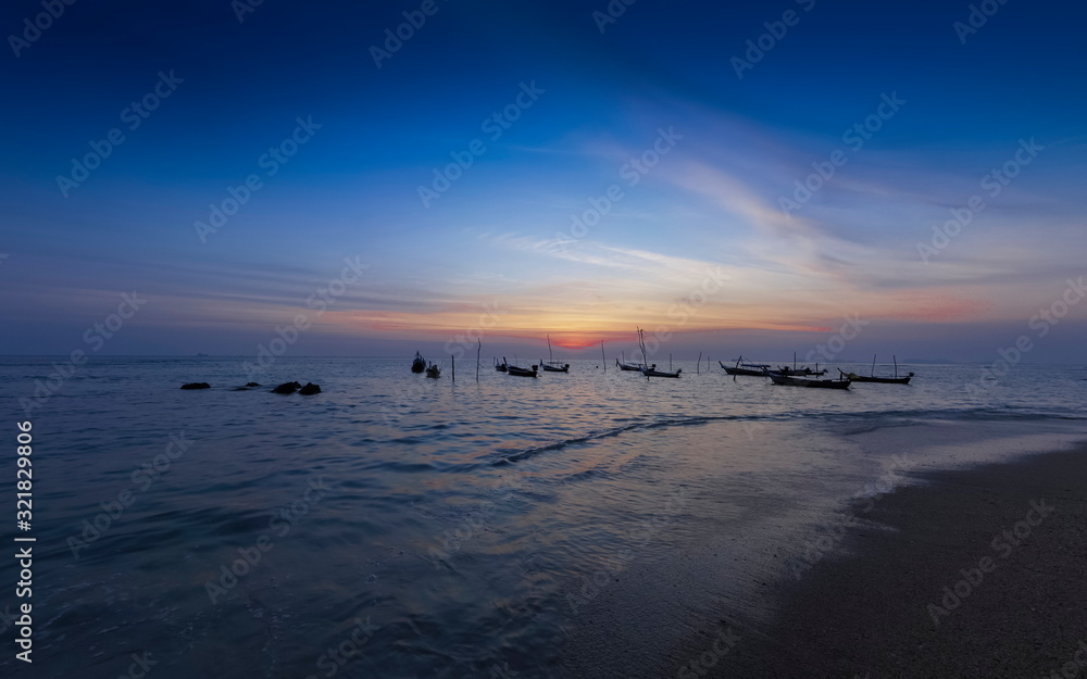 view seaside evening of fishing boats floating in the sea with orange sun light and blue sky background, sunset at Klong Hin Beach, Ko Lanta island, Krabi, southern of Thailand.