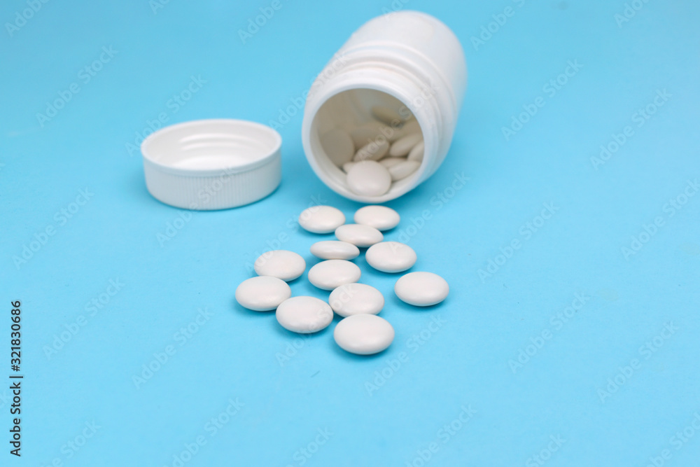 Close up white pills spilled out medication bottle on blue background. Health care pharmacology concept Close up white pills spilled out medication bottle on blue background. Health care pharmacology concept
