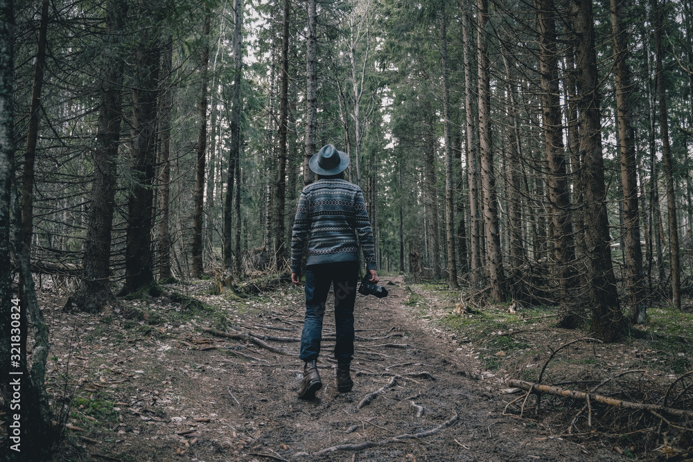 Obraz premium Man traveler with photo camera walking in the dark forest. Travel Lifestyle and Adventure concept.