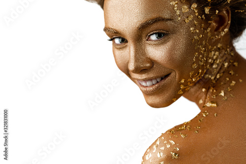 Fototapeta Fashion art portrait of model girl with holiday golden shiny professional makeup. beaty smiling woman with gold metallic body and hair on white background. Gold glowing skin. copy space