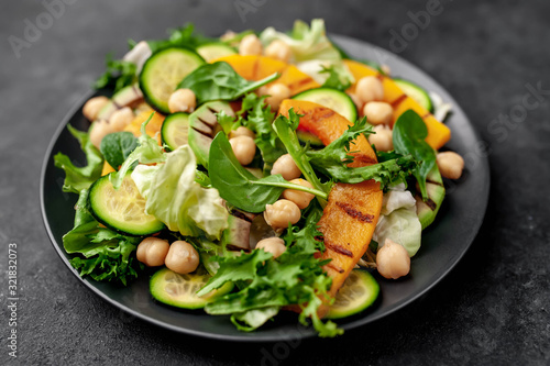 plate of pumpkin salad, avocado, cucumber, chickpeas, lettuce on a stone background.