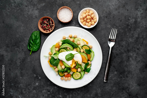 a plate of avocado salad, chickpeas, pumpkin, cucumber, poached egg in a plate on a stone background