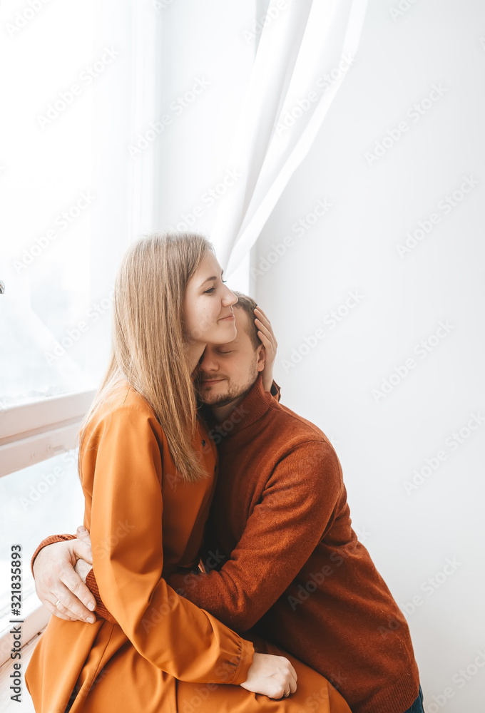 Young couple in love embracing near window at home. Vertical portrait Young couple in love embracing near window at home. Vertical portrait