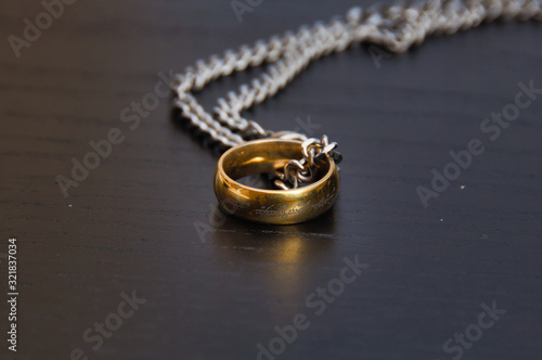 Golden ring with chrome chain on black wooden surface.