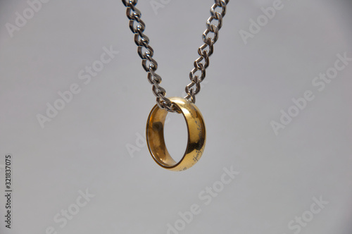 Golden ring hanging in the air from chrome chain on white background.