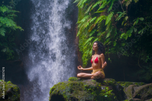 outdoors portrait of young attractive and happy hipster girl doing yoga at beautiful tropical waterfall meditating enjoying freedom and   nature in wellness and zen lifestyle