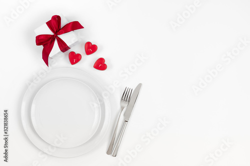 Valentines day or romantic dinner background. Festive romantic table setting with candles in the shape of hearts and a gift on a white background.