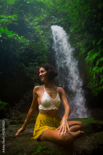 outdoors portrait of young attractive and happy hipster woman doing yoga at beautiful tropical waterfall meditating enjoying freedom and   nature in wellness and zen lifestyle