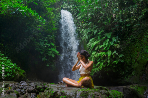 outdoors portrait of young attractive and happy hipster woman doing yoga at beautiful tropical waterfall meditating enjoying freedom and   nature in wellness and zen lifestyle