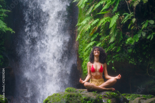 outdoors portrait of young attractive and happy hipster woman doing yoga at beautiful tropical waterfall meditating enjoying freedom and   nature in wellness and zen lifestyle