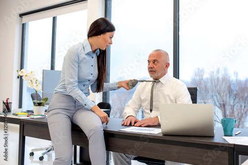 Attractive businesswoman draws senior colleague for his tie in the office