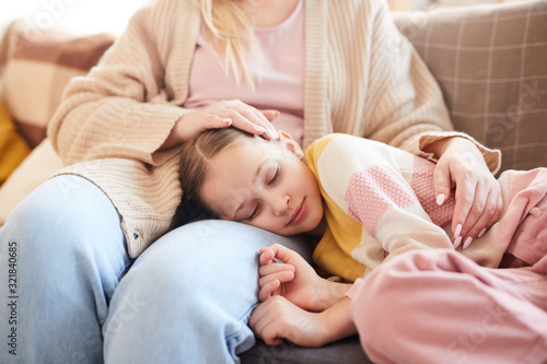 Warm-toned portrait of cute girl sleeping on mothers lap while lying on couch at home, copy space
