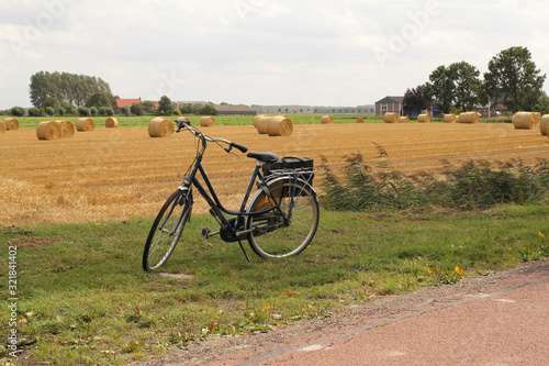 a bicycle in front of a field with round straw bales in the dutch countryside in springtime © Angelique