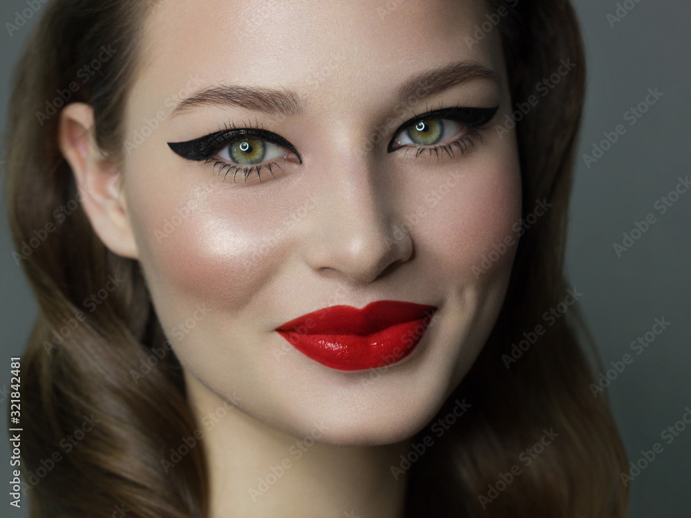 Beautiful brunet model woman face with green eyes and perfect make-up make smile on camera. Portrait of beauty with red lips and eyes liner, thick eyesbrow . Female face with clear skin close-up. Beautiful brunet model woman face with green eyes and perfect make-up make smile on camera. Portrait of beauty with red lips and eyes liner, thick eyesbrow . Female face with clear skin close-up.
