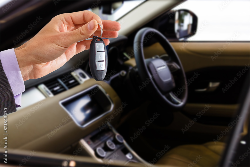 Smiling car salesman handing over your new car keys, dealership and sales concept