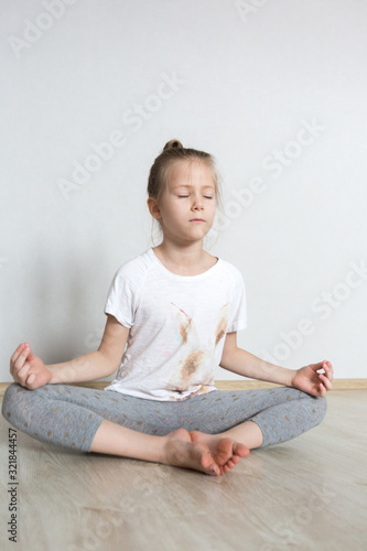 A little cute girl practices a yoga pose indoors. The child does yoga and gymnastic exercises.