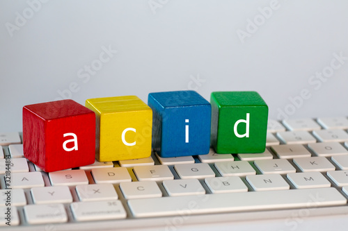 The letters acid stands for  Atomicity Consistency Isolation and Durability was written on blocks. Letters are written in white on red, yellow, blue and green blocks and stand on a bright computer photo