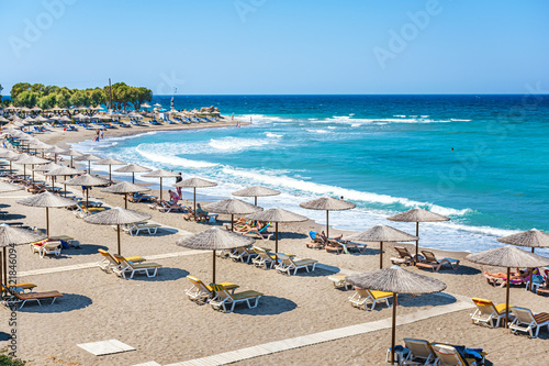 Beach with people, umbrellas and sunbeds near ancient city of Kamiros (Rhodes, Greece)