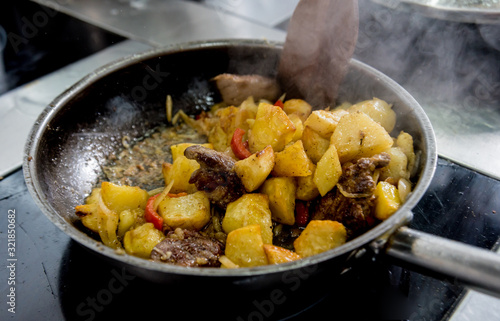 Chef cooks fried potatoes with pieces of meat in a restaurant kitchen