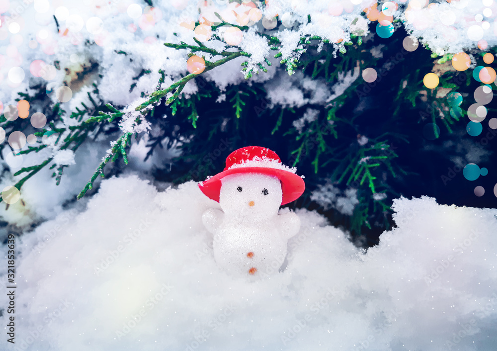 Christmas and Happy New Year composition of cute snowman in red hat standing in the snow near the christmas tree. Shining colored round glare. Celebration background with copy space for your text