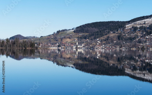 Schliersee in Oberbayern. Panorama von Fischhausen am Horizont mit lichtreflexion am see, Ort im Winter mit Kirchdorf Sankt Sixtus