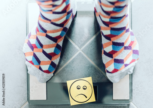 close-up of person in socks on bathroom scale with unhappy smiley face, overweight concept