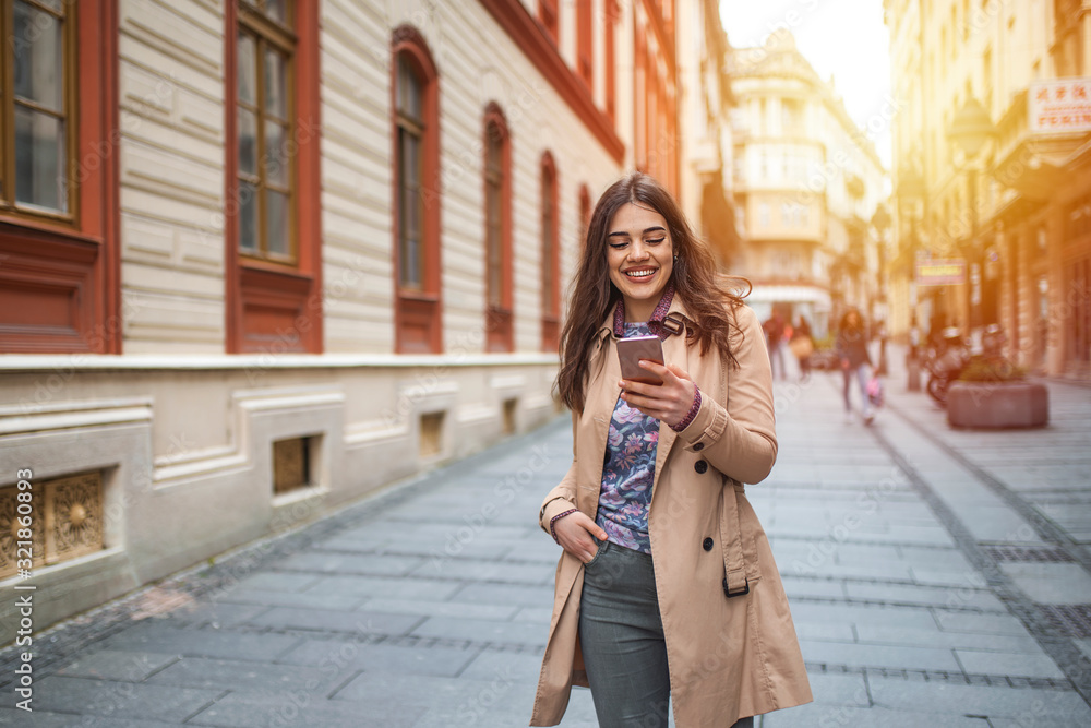 Portrait of young happy woman walking in city and using smartphone. Girl browse the Internet. Happy and funny woman looking at her phone. Caucasian woman female using smartphone walking streets Portrait of young happy woman walking in city and using smartphone. Girl browse the Internet. Happy and funny woman looking at her phone. Caucasian woman female using smartphone walking streets