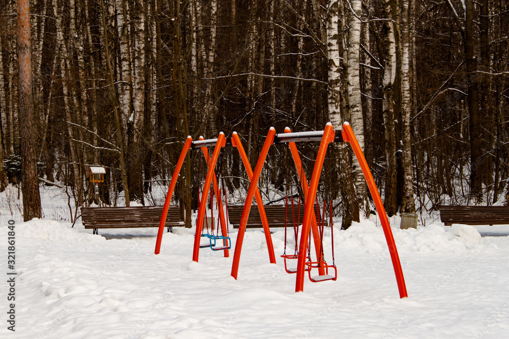 Two red double children swing on the playground on winter day in park background Two red double children swing on the playground on winter day in park background