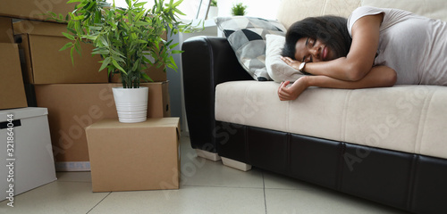 Tired preparing to move, woman sleeping on couch. Young dark-skinned woman is waiting for transportation service, next to are cardboard boxes with things. Items packed in boxes are ready to move.