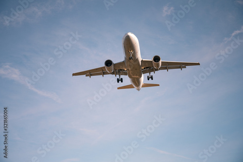 Low-angle view of passenger airplane with landing gear before touchdown at airport against blue sky with clouds