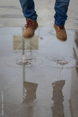 Water and fund with booths. Kid is jumping and splashing on a water mud in the street, wearinf jeans and brown boths photo