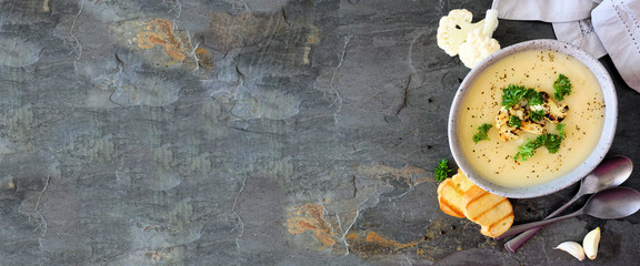 Roasted cauliflower and potato and soup. Above view banner with side border over a dark stone background with copy space.