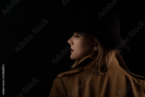 Retro gangster woman in a brown cloak and black hat. Photoshoot in the style of the mafia. Dark blurred background, blurred focus, noise.