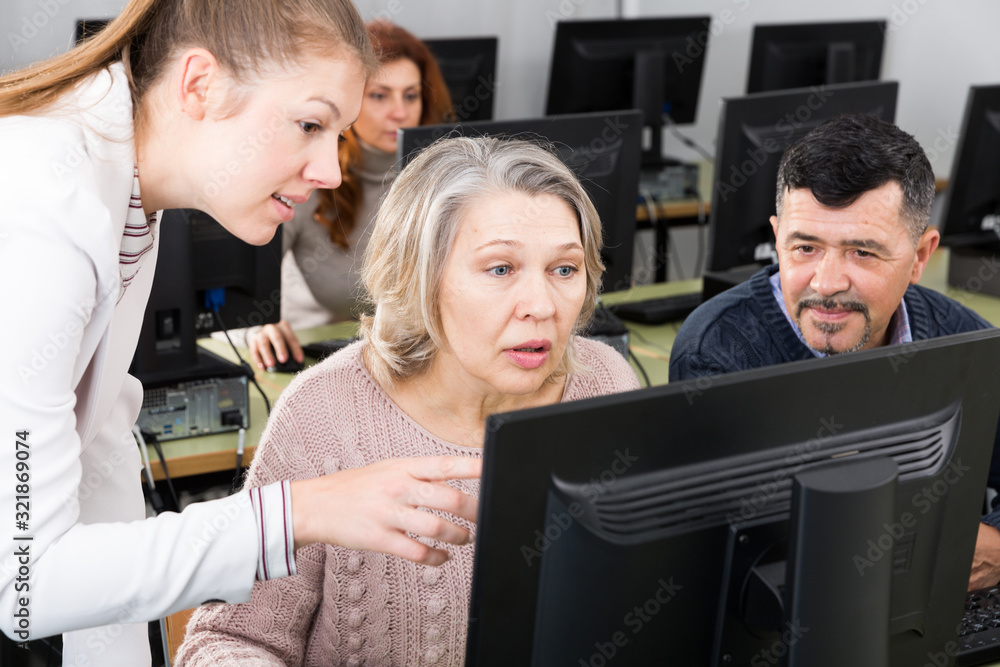 Obraz premium Young female teacher helping mature people to use computer