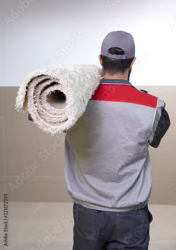 Man wearing uniform standing with a roll of carpet on his shoulder, back view photo