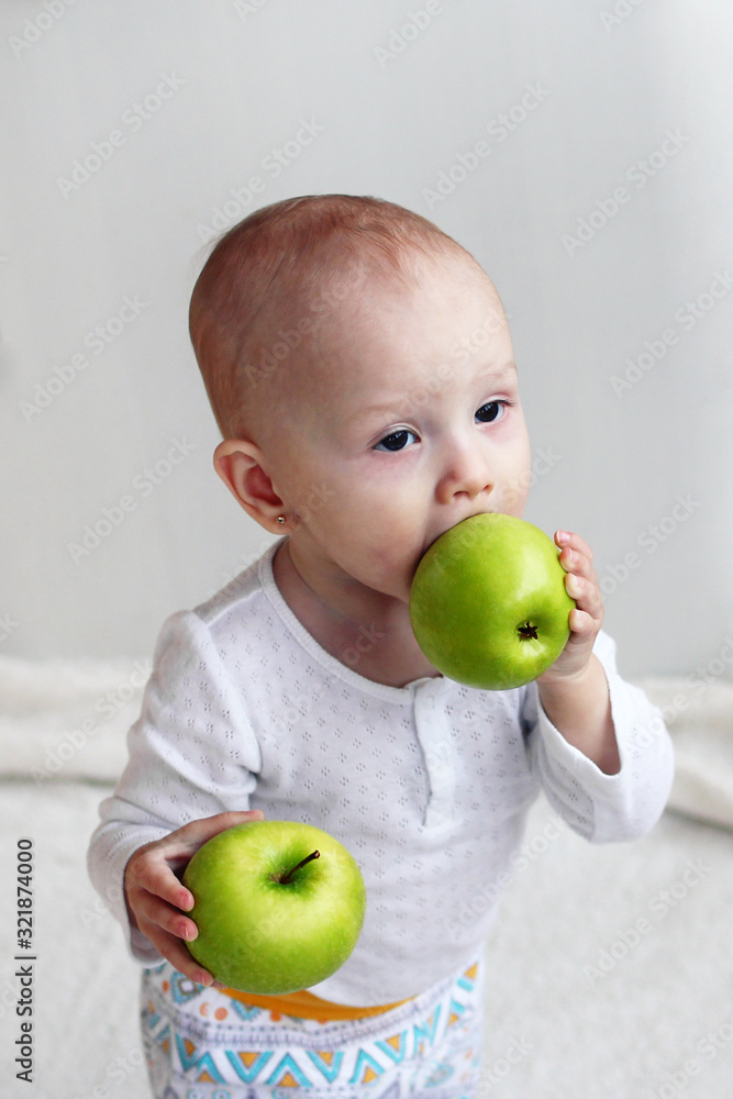 Little girl is holding in hands two green apples and trying to bite off one of them. Little girl is holding in hands two green apples and trying to bite off one of them.